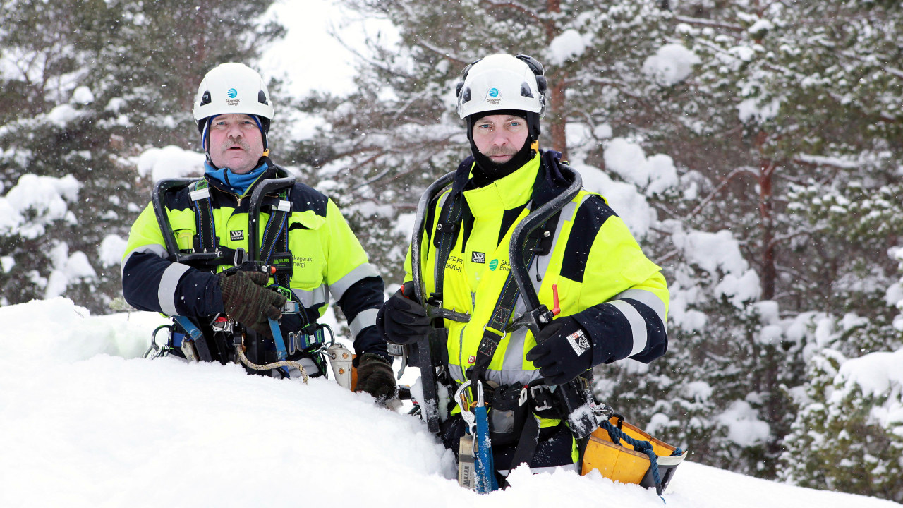 To energimontører står med snø til livet i fullt arbeidsantrekk. Foto