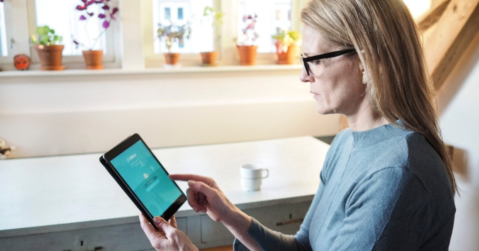 En dame led langt lyst hår og briller ser på en iPad.