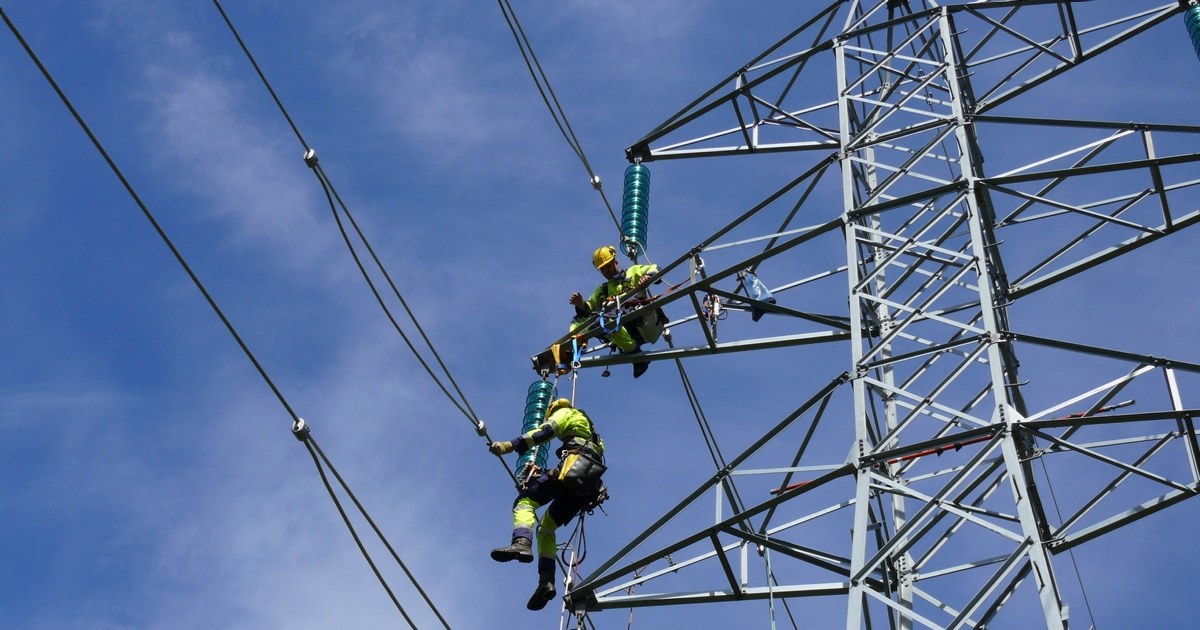To energimontører klatrer i en kraftmast.