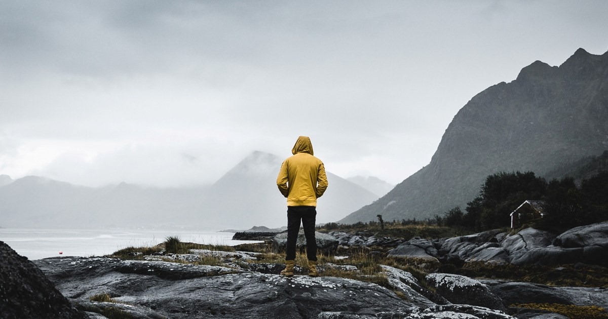 Mann i gul regnjakke står i fjæra og ser utover havet.