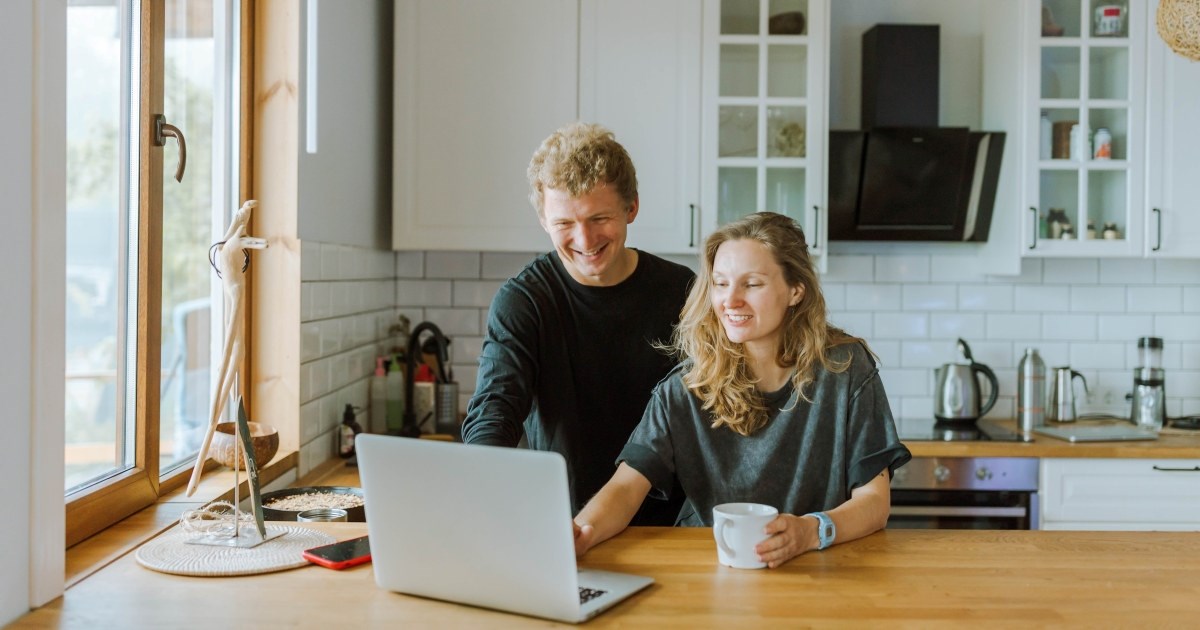 En mann og en dame er på kjøkkenet og ser på en PC. Foto