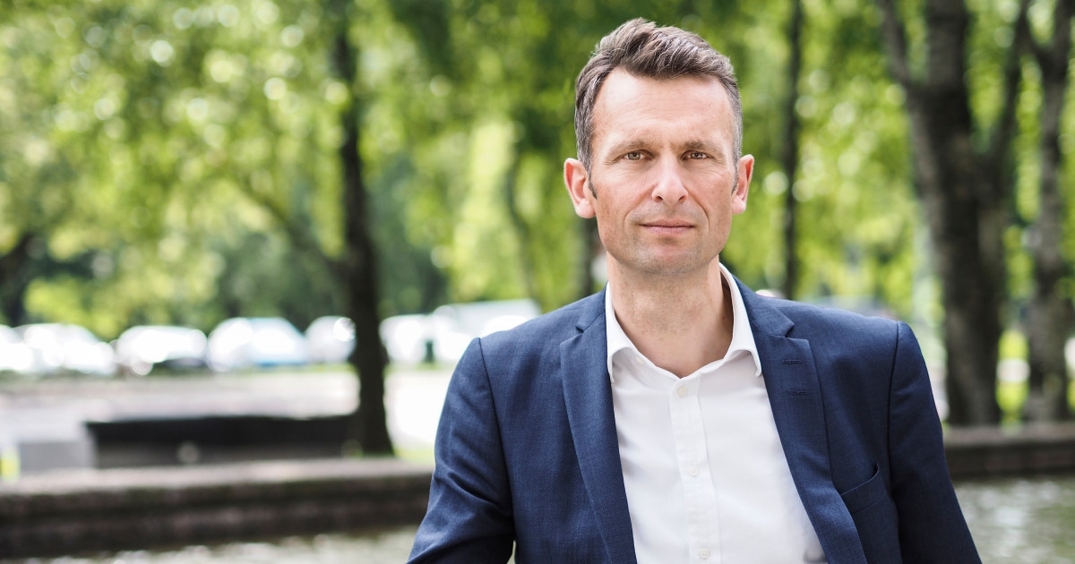 Foto: Knut Kroepelien står foran et basseng med grønne trær i bakgrunnen.